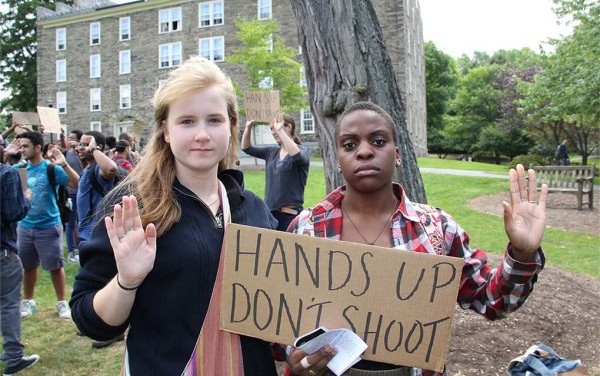 Students raise their hands while displaying a sign that reads hands up, don't shoot