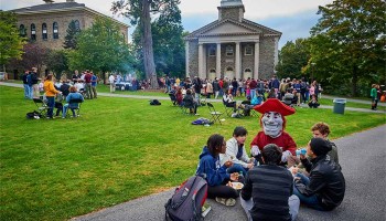 Raider sits with students eating on the Academic Quad