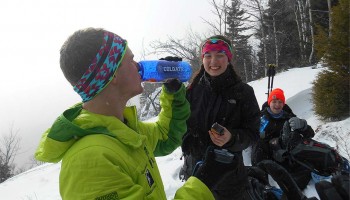 Student in snow gear drinks from a Colgate water bottle among friends