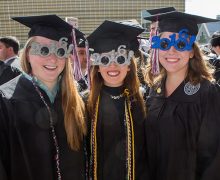 Three female graduates in caps and gowns wear 2016 sunglasses